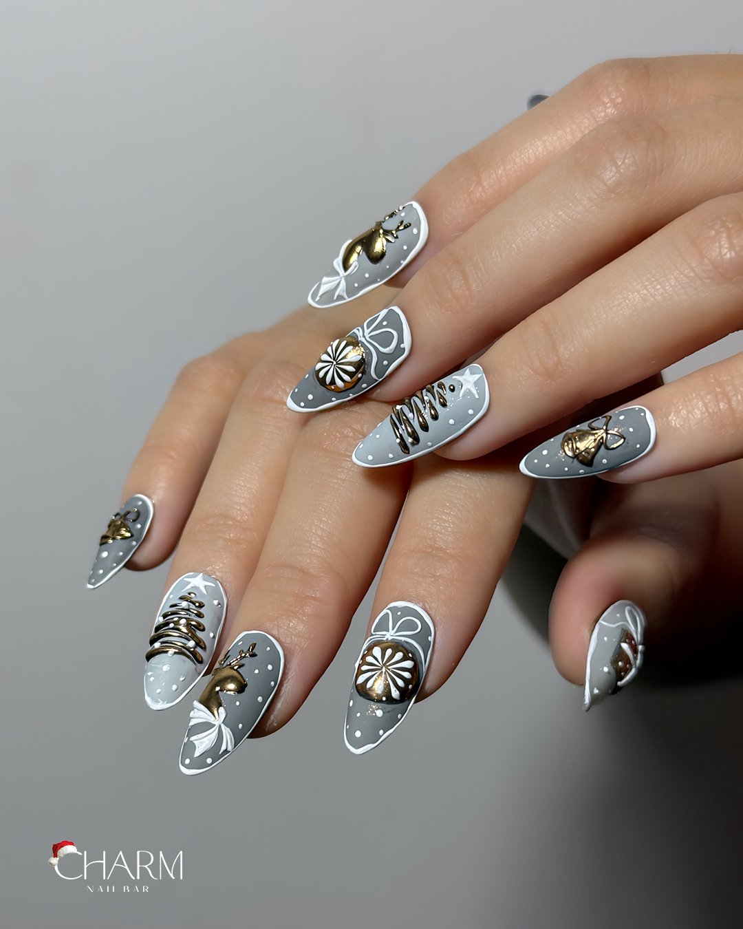 A close-up photograph of a hand displaying intricately designed nail art featuring various patterns and embellishments in shades of grey with metallic