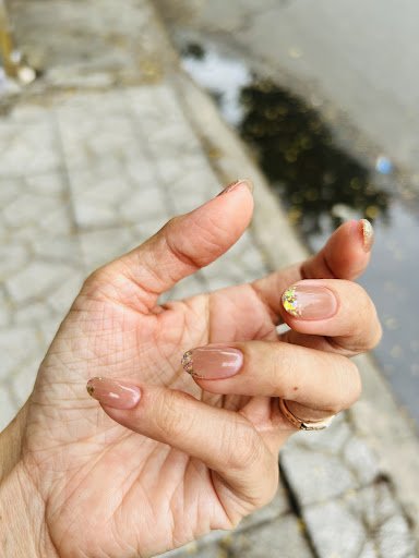 A close-up of a person's hand displaying manicured nails against an outdoor urban background with pavement and water puddles visible.