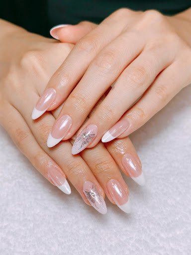 A close-up photograph of a pair of hands displaying intricately designed nail art featuring shades of pink and white with decorative patterns on the t