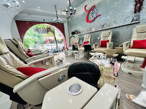 The image depicts an interior view of a modern nail salon or beauty spa. The space is well-lit with natural light coming through the large windows, an