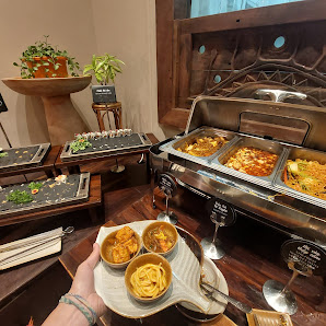 The image depicts an interior dining area at a venue in Thao Dien, Saigon. A person holds a plate with multiple dishes, likely Vietnamese cuisine, inc