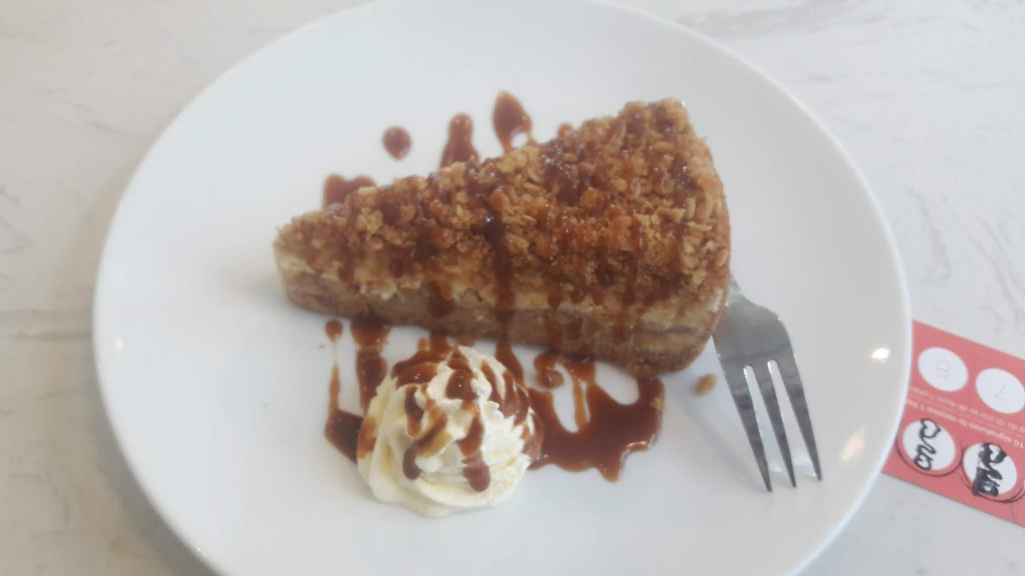 A slice of caramelized dessert topped with a crumbly topping and drizzled with sauce on a white plate, accompanied by a scoop of vanilla ice cream wit