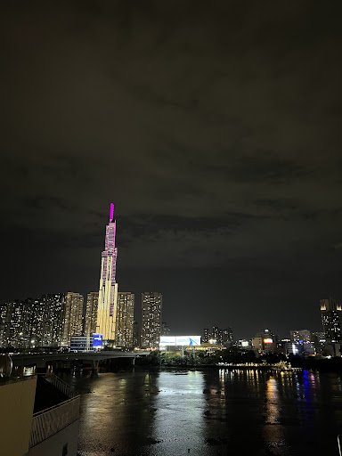 Night view of Saigon's skyline from Thao Dien, featuring the Bitexco Financial Tower with purple lighting, surrounding high-rise buildings, a river re
