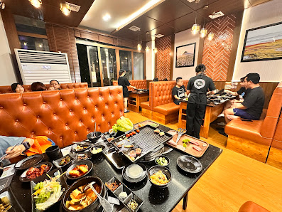 A bustling restaurant interior in Thao Dien, Saigon, featuring brown tufted leather booths, wooden tables, and a black table filled with various dishe