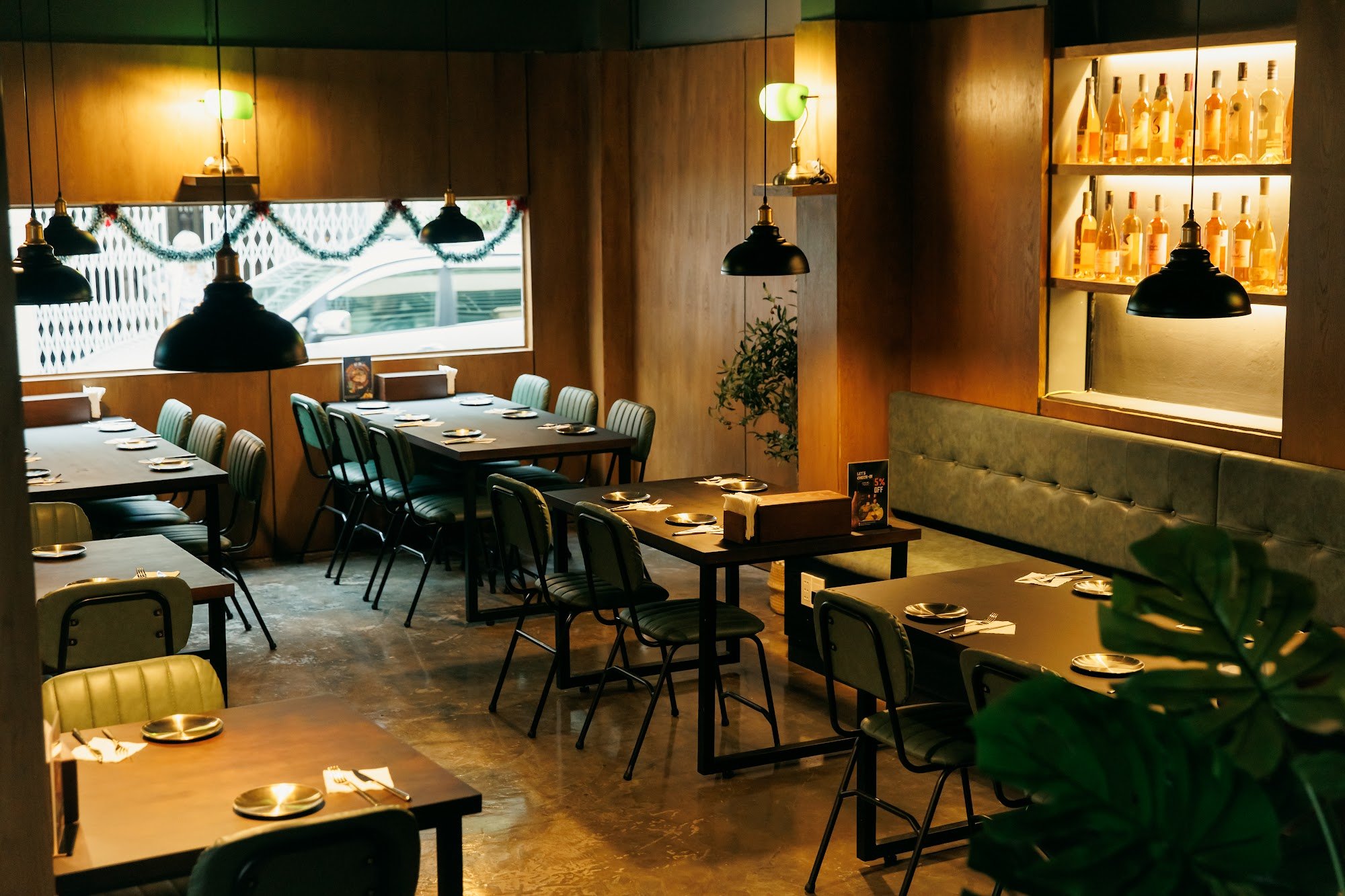The image depicts the interior of a modern restaurant in Thao Dien, Saigon. It features wooden paneled walls, dark wooden tables, and green upholstere