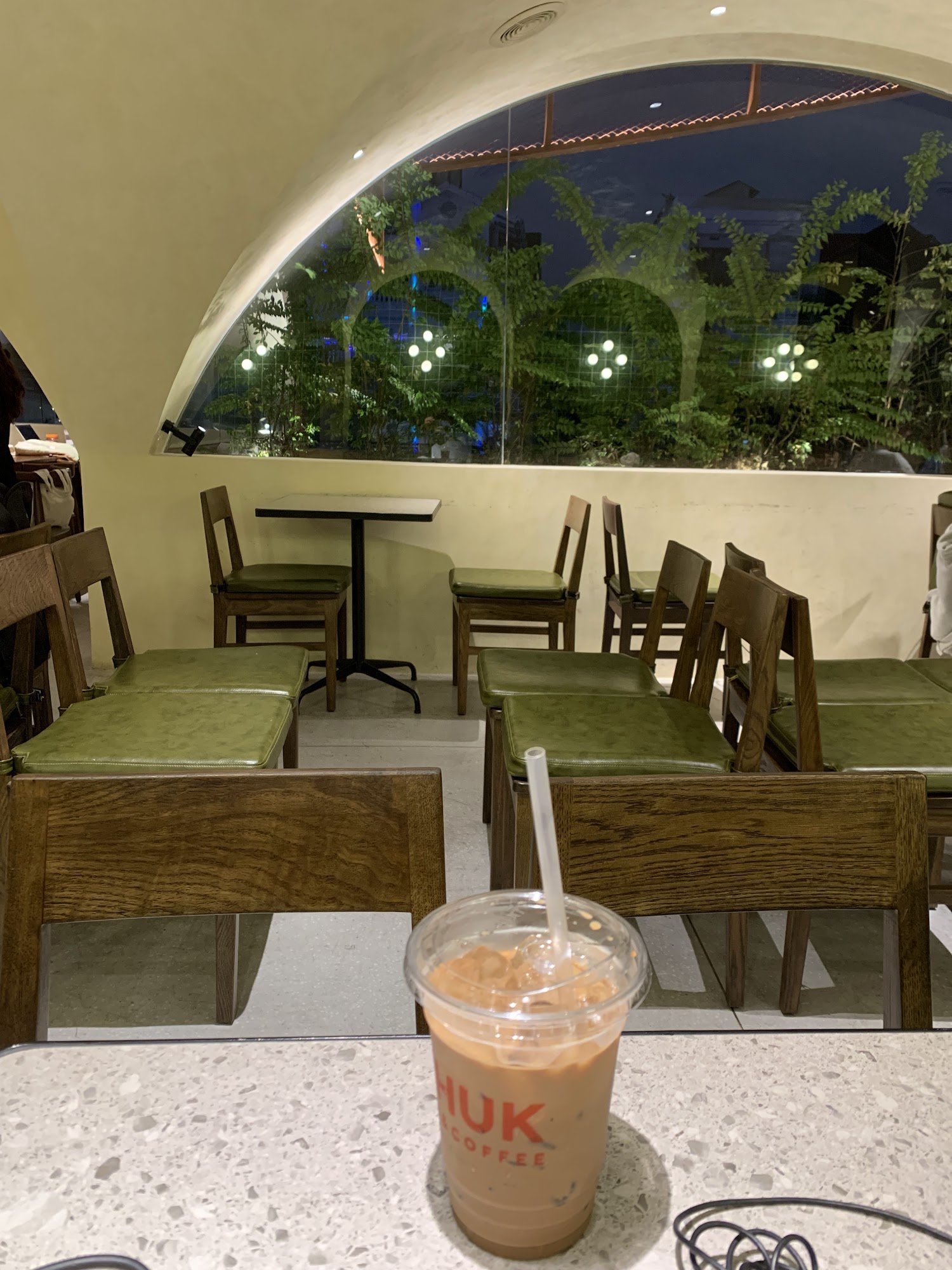 The image shows an interior view of a cafe or restaurant named 'NUK Coffee'. The setting appears to be during the evening, as indicated by the dark sk
