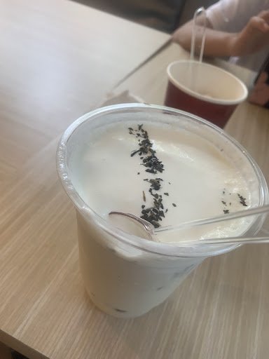 A close-up of a plastic cup containing a white beverage sprinkled with what appears to be black tea leaves on top.