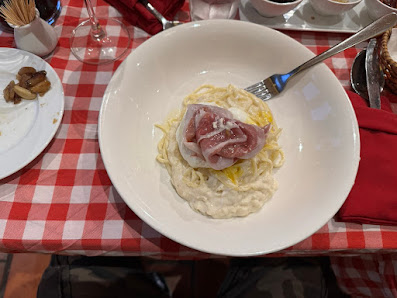 A plated dish consisting of a slice of raw meat on top of what appears to be creamy risotto or polenta, served in a white bowl with a fork resting bes