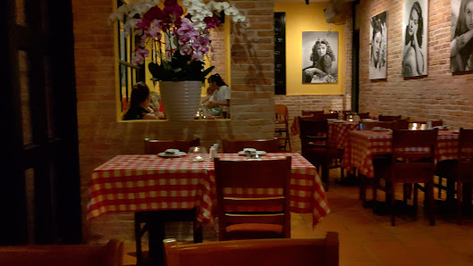 The image depicts an interior view of a cozy restaurant featuring brick walls adorned with framed black and white photographs. The space is warmly lit