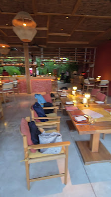 An indoor dining area with wooden tables and chairs, featuring several tables set with plates, candles, and cushions on the chairs. The ceiling has a 