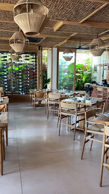 A spacious restaurant interior in Thao Dien, Saigon, featuring wooden tables and chairs, woven pendant lights, large windows with greenery outside, an