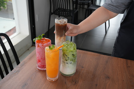 A person is holding a tall glass of dark brown beverage among three other drinks on a wooden table in an indoor setting.