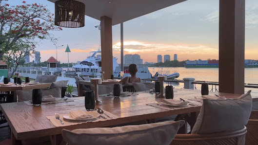 The image depicts an outdoor dining area at sunset in Thao Dien, Saigon. The tables are set with dinnerware and glasses on a wooden deck overlooking t
