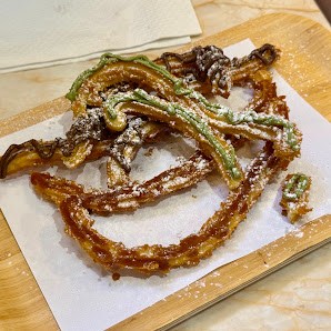 A close-up of a dish consisting of what appears to be fried dough or pastry strips topped with green and brown sauce, sprinkled with powdered sugar.