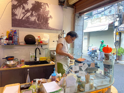 A person is cooking at a food stall in an interior setting that appears to be part of a larger establishment with various items on display and contain