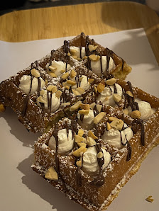 A close-up of a dessert consisting of waffles topped with whipped cream and chocolate syrup drizzled over the top, garnished with nuts.