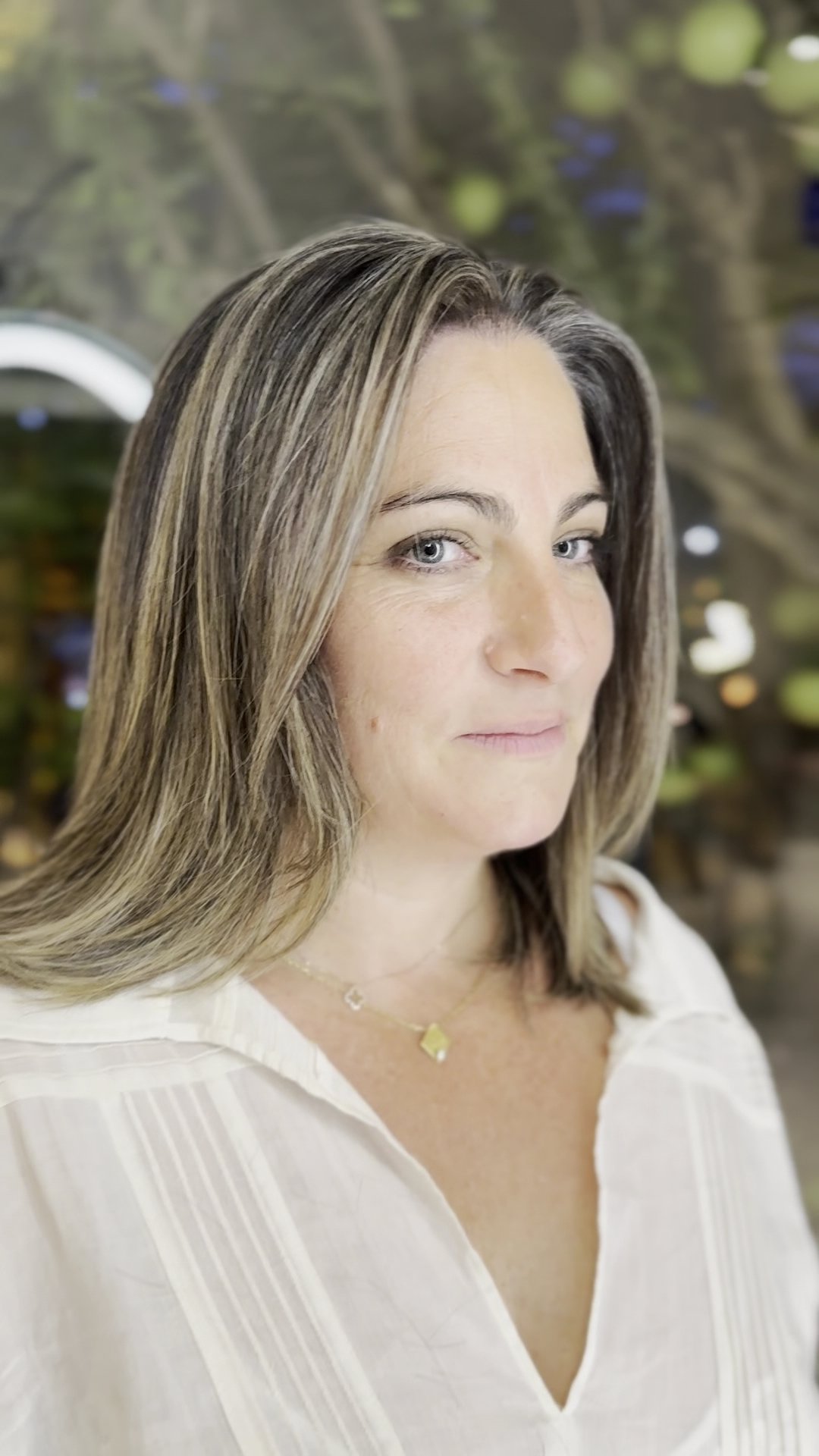 A woman is captured in a close-up portrait wearing a white blouse and delicate jewelry.