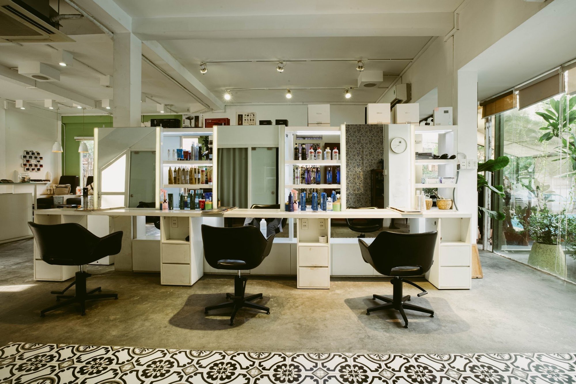 A modern hair salon interior in Thao Dien, Saigon, featuring white styling stations with black swivel chairs, shelves stocked with various hair care p
