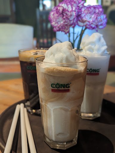 The image shows a close-up of three glasses containing frothy beverages from the brand 'CONG'. The drinks appear to be coffee-based, with one having w