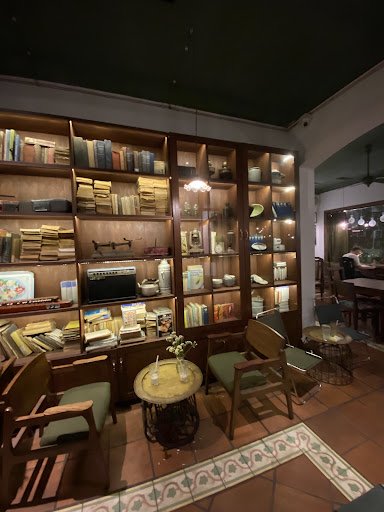 The image depicts an interior space that appears to be a cozy bookstore or library café with wooden shelves filled with books and various decorative i