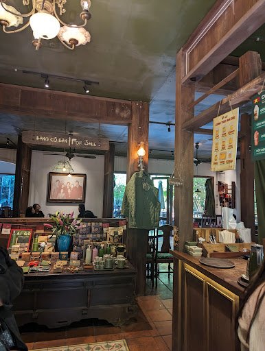 The image depicts an interior view of a cozy store or café featuring rustic wooden decor and various items for sale on display, including books, candl