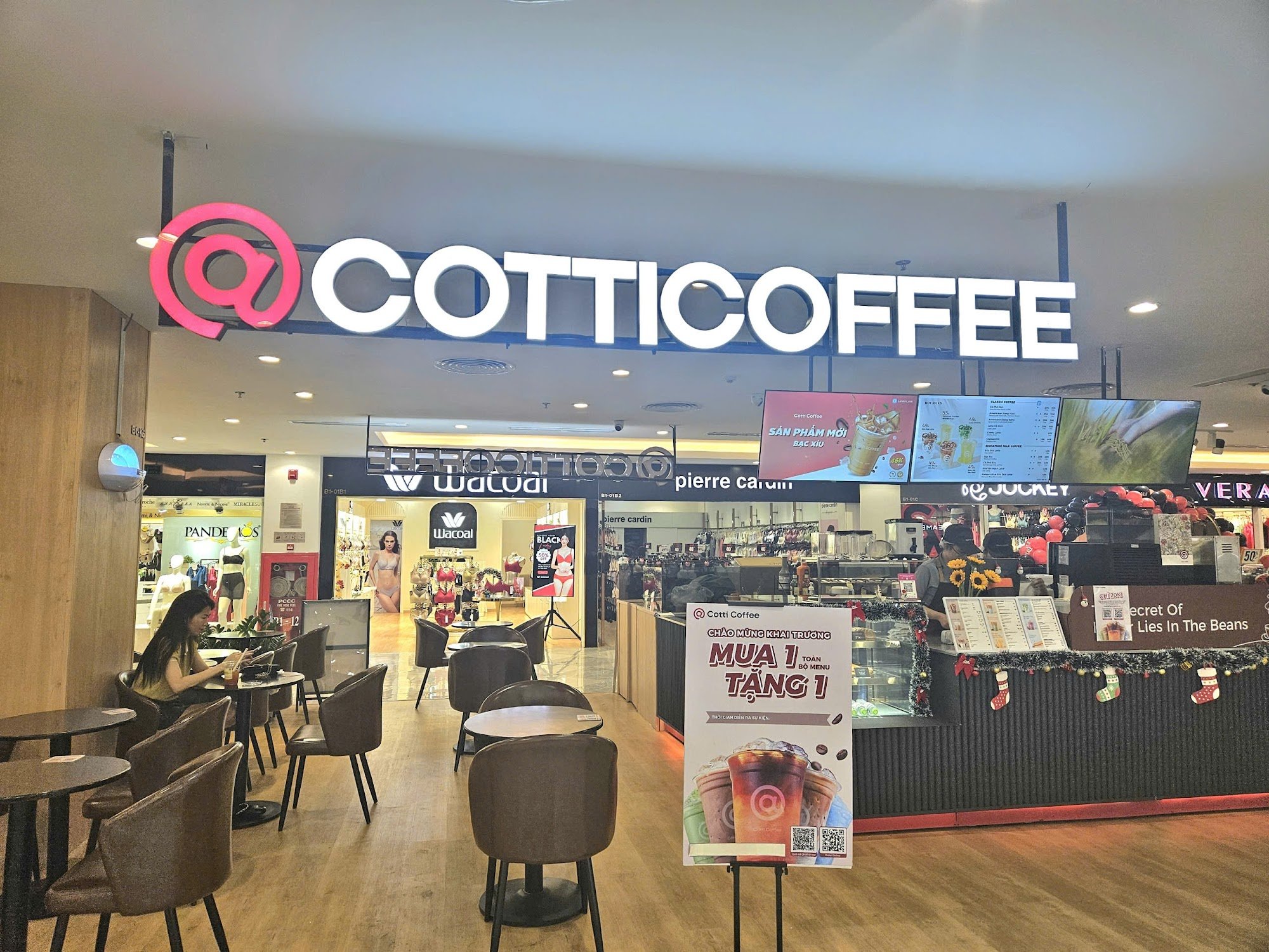 The image shows an interior view of a coffee shop named 'Cotti Coffee'. The establishment has modern decor with wooden flooring and dark-colored chair