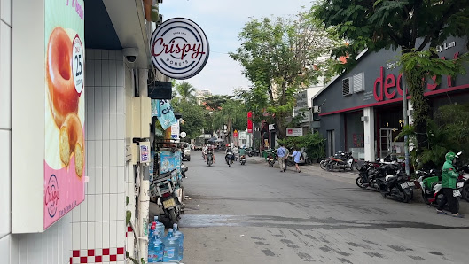 The image depicts a street view of an urban area in Thao Dien, Saigon with various shops and eateries on the left side including 'Crispy' which appear