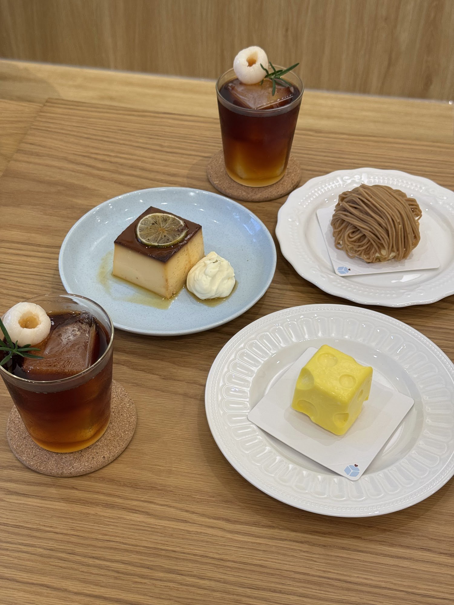 The image shows a selection of desserts and beverages on a wooden table in what appears to be an indoor setting with warm lighting, likely within Thao