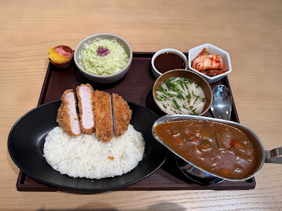 A tray of Japanese cuisine including rice topped with fried pork cutlets (katsu), a side dish of shredded cabbage, kimchi, pickled radish, and two typ