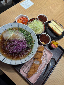The image shows a meal consisting of various dishes served on a tray. There is a bowl with what appears to be ramen topped with purple cabbage and gre