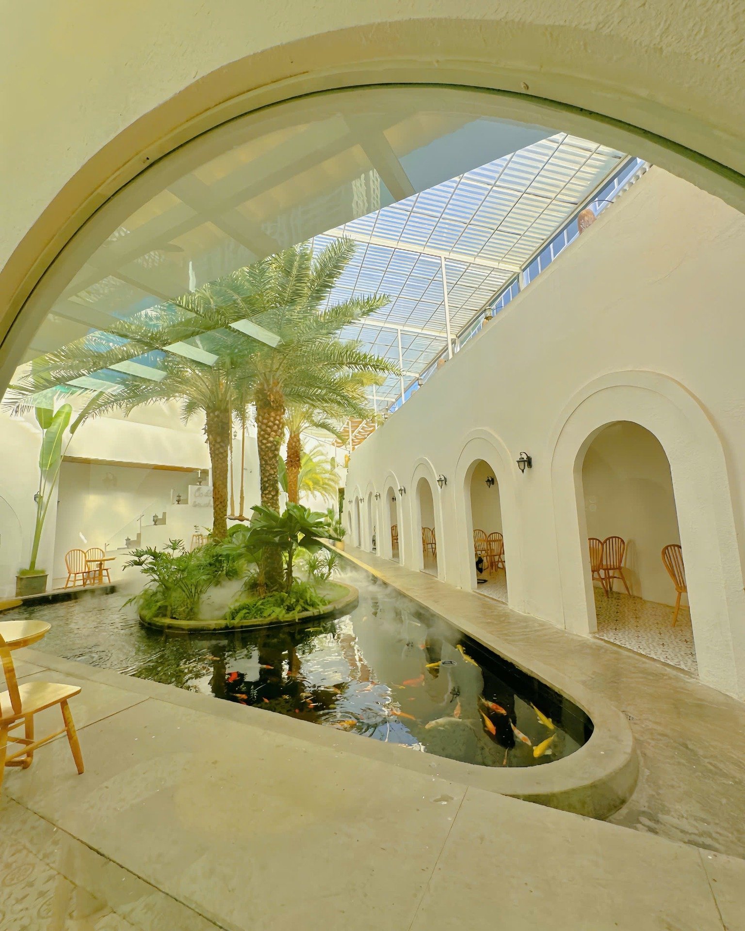 The image shows an indoor courtyard area of a venue named Thao Dien in Saigon. It features white arches leading to various seating areas, with lush gr