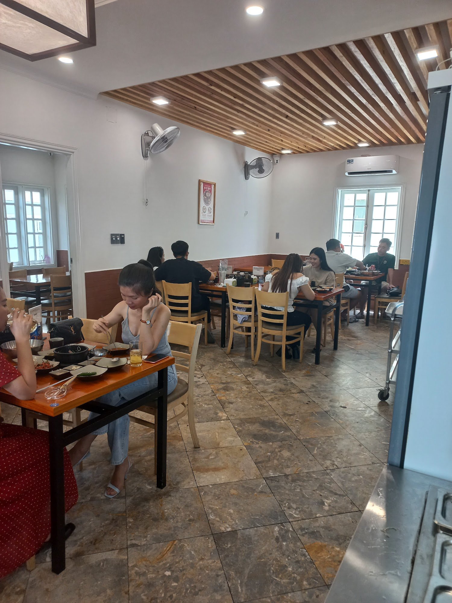 The image depicts an indoor dining area in a restaurant or cafe setting. The interior features wooden slatted ceilings and tiled flooring, with variou
