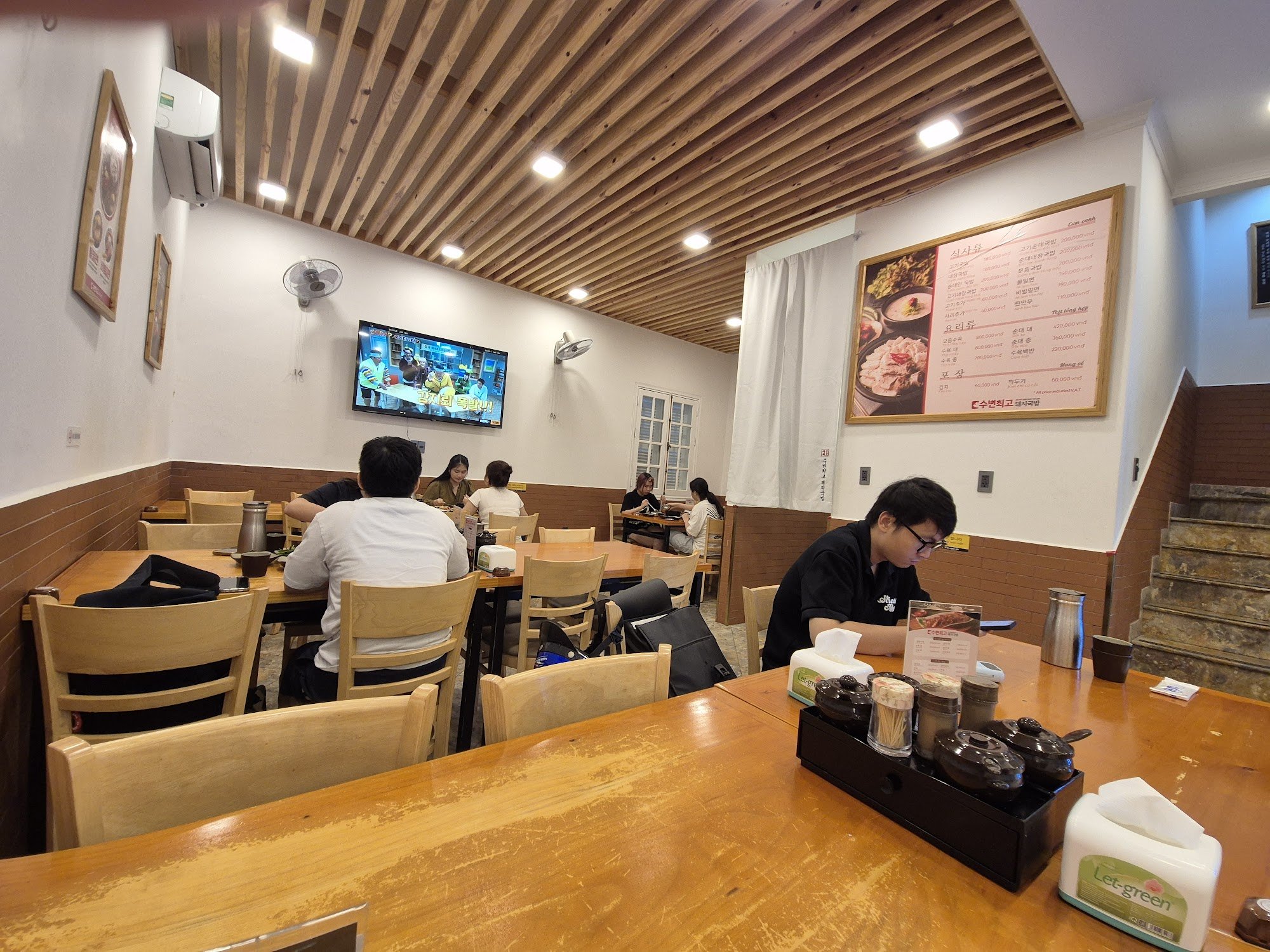 The image shows an interior view of a casual dining restaurant in Thao Dien, Saigon. The decor includes wooden slatted ceilings and walls with white p