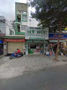 The image shows an exterior view of a pharmacy named 'MY DUC' located on the ground floor of a building in Thao Dien, Saigon.