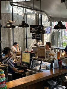 The image depicts an interior view of a cafe or restaurant at Thao Dien, Saigon. The setting includes a counter with staff working on computers and ha