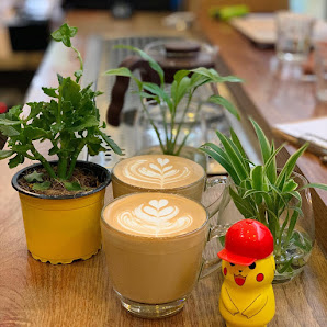 The image shows a cozy interior setting of what appears to be a café or coffee shop with various items on the counter, including two cups of latte art