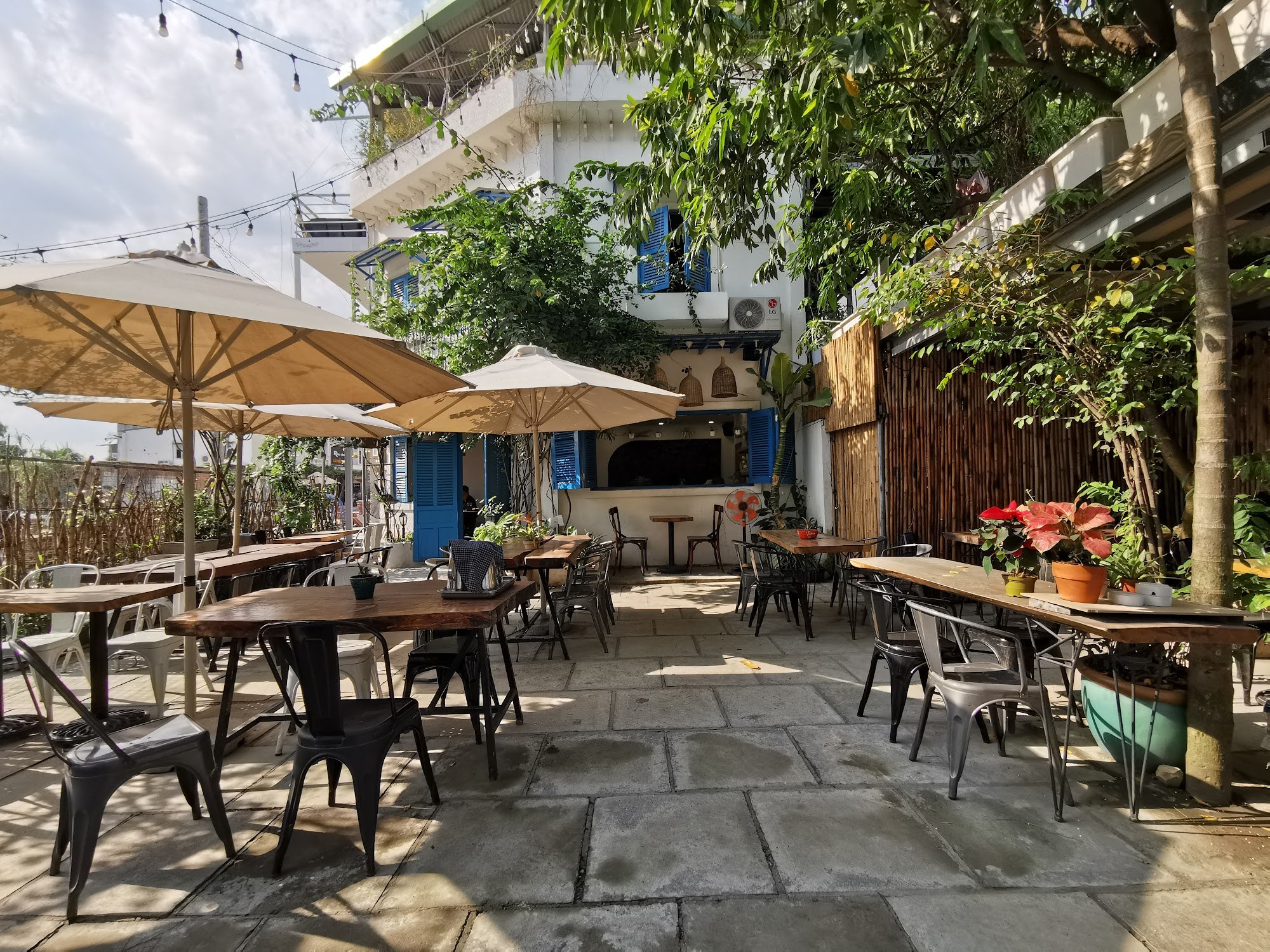 This image depicts an outdoor seating area of a restaurant or café in Thao Dien, Saigon. The setting includes several wooden tables and chairs with la