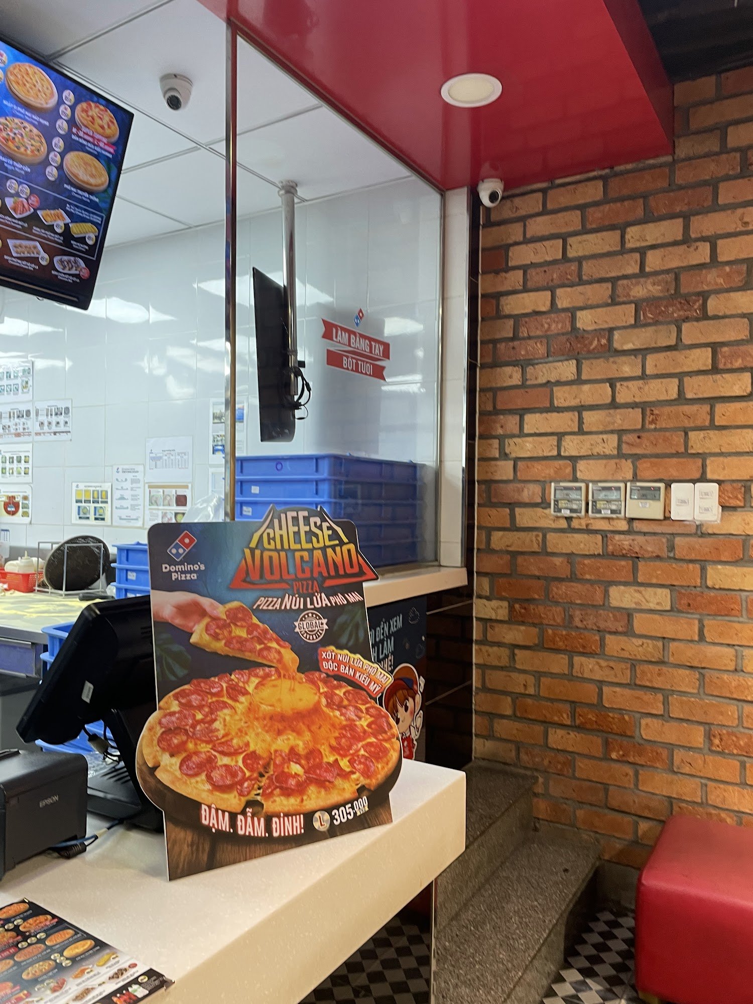 The image shows an interior view of a Domino's Pizza restaurant in Thao Dien, Saigon. The focus is on the ordering counter area with promotional signa