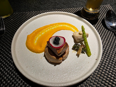 A plated dish featuring a stack of meat and vegetables on top of what appears to be slices of bread or toast, accompanied by asparagus spears, green b