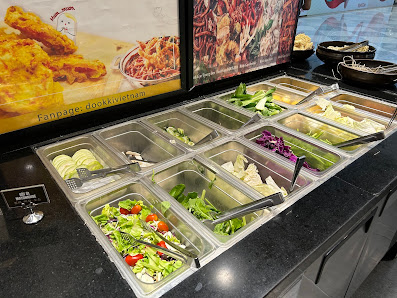The image depicts a buffet-style food counter in a restaurant located in Thao Dien, Saigon. The counter features multiple stainless steel containers f