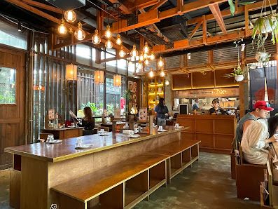 The image depicts the interior of a modern café or restaurant in Thao Dien, Saigon. It features a long wooden counter with a bench seating area, multi