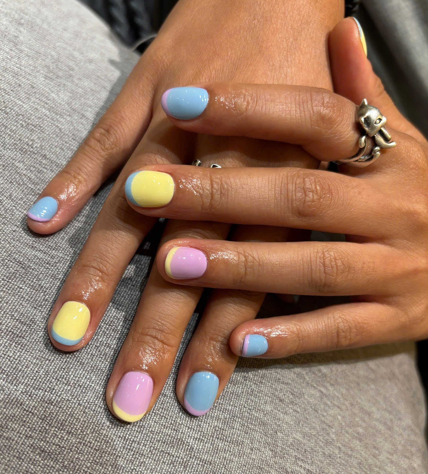 A close-up of a person's hands displaying colorful nail polish in pastel shades on each fingernail.