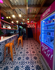 The image shows an interior view of a restaurant named 'Tacos Heaven'. The establishment has a retro vibe with colorful neon lights and tiled flooring