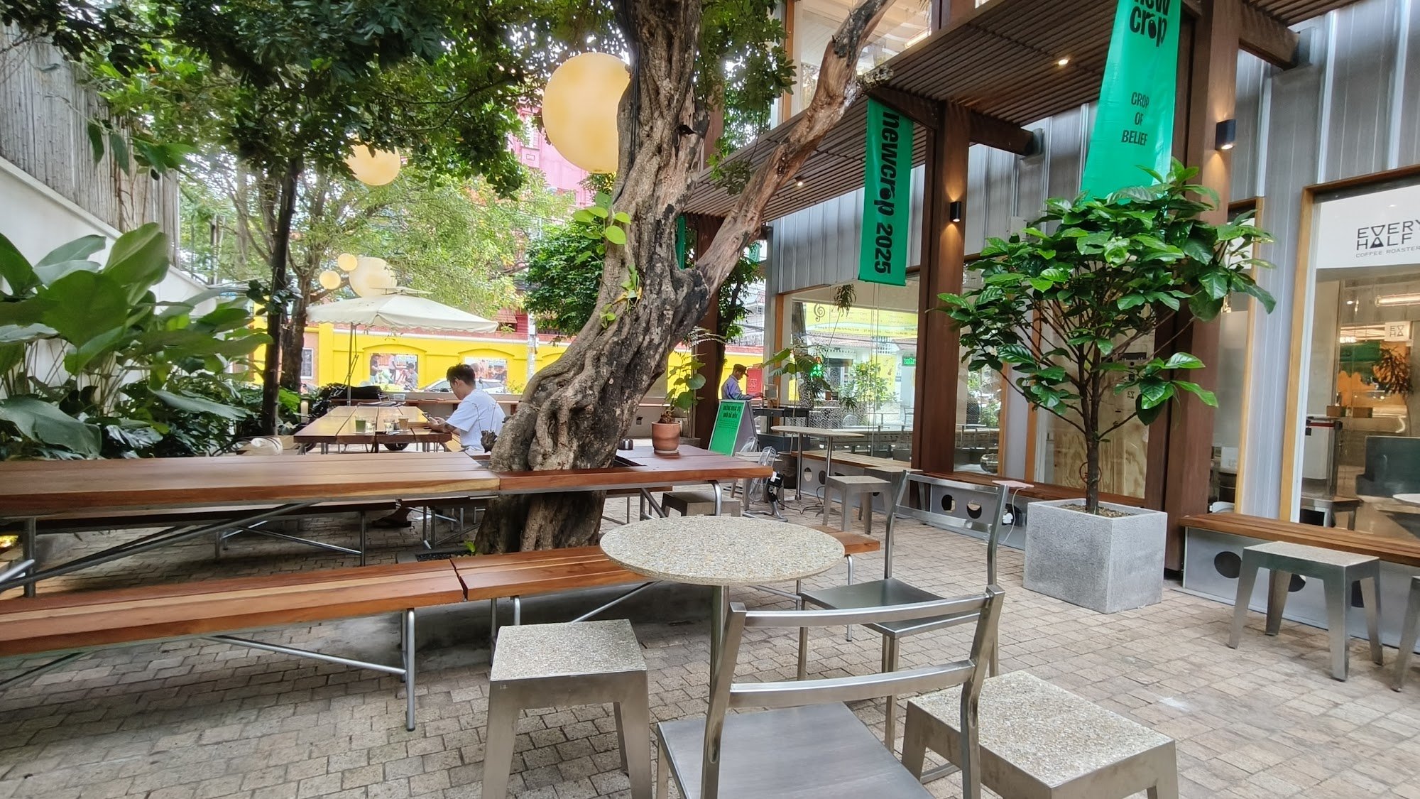 The image shows an outdoor seating area of a cafe or restaurant located in Thao Dien, Saigon. The space is designed with modern and casual elements fe