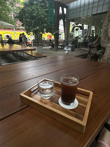 The image shows a wooden table in an outdoor seating area of Thao Dien, Saigon with two beverages on a tray: one appears to be tea and the other is wa