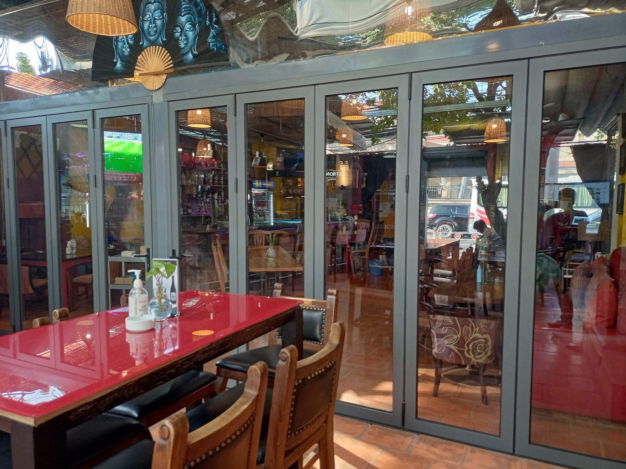 The image depicts the interior of a restaurant or café in Thao Dien, Saigon. It features a red table with black cushioned chairs, glass doors leading