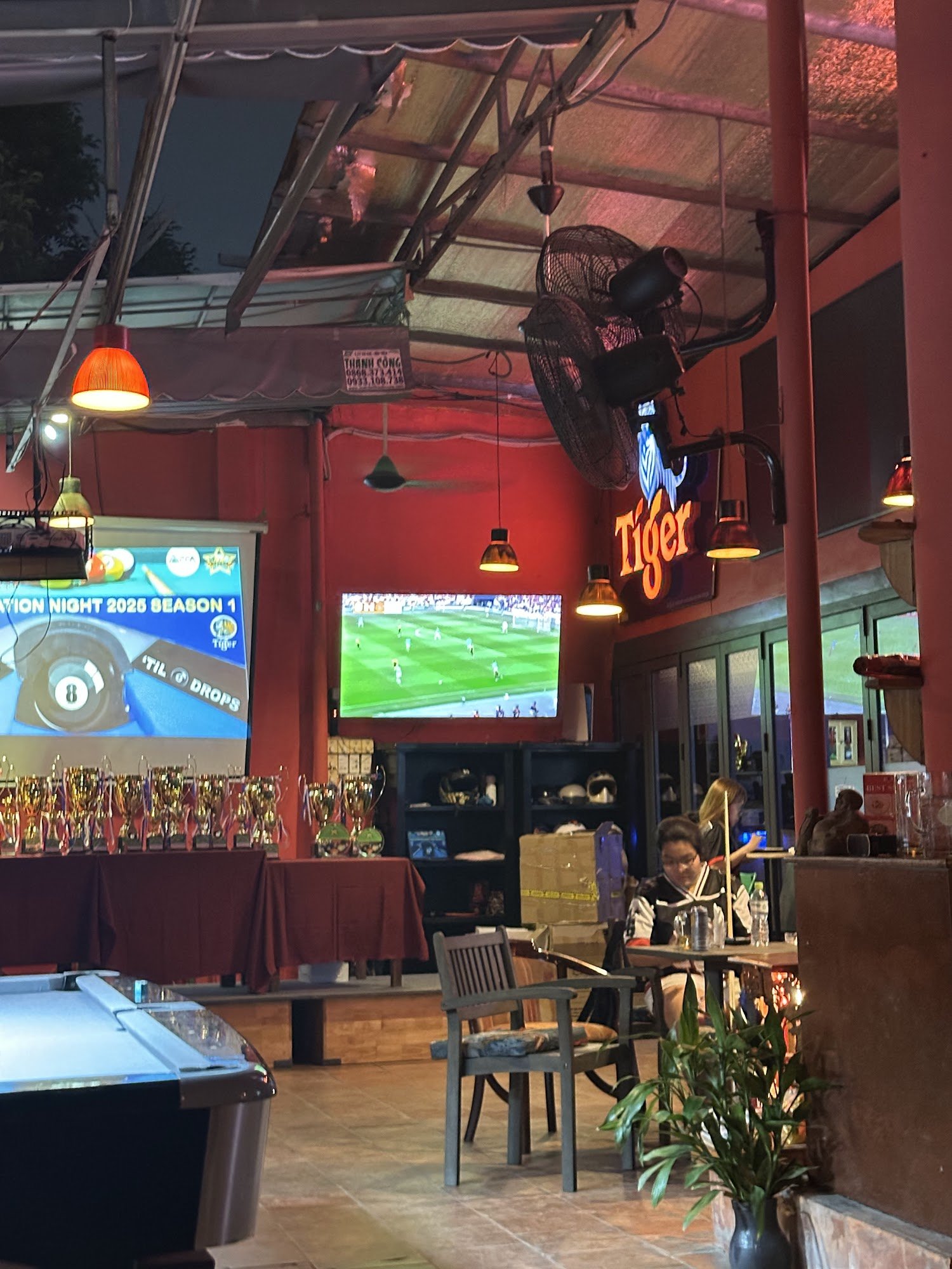 The image shows an indoor sports bar or pub named 'Tiger' in Thao Dien, Saigon. The venue features a red and orange color scheme with various seating