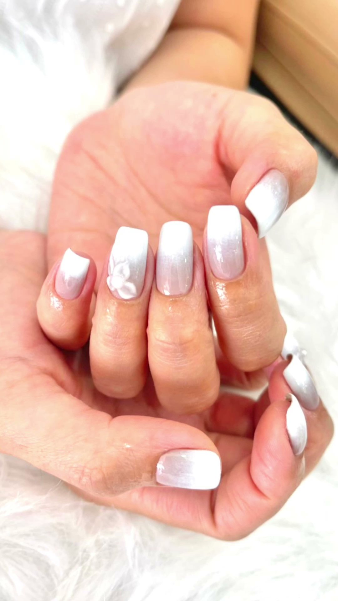 A close-up of a person's hand displaying well-manicured nails painted in various shades of white and silver with some decorative elements on the tips.