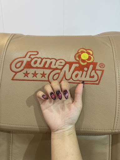 A close-up of a hand resting on the armrest of an upholstered chair with 'Fame Nail' branding in red and yellow, indicating it is likely located withi