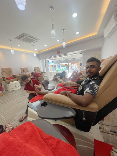 The image shows an interior view of a nail salon or spa where several individuals are seated in reclining chairs receiving pedicures.